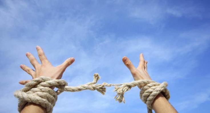 Hands breaking free from rope against a clear blue sky.